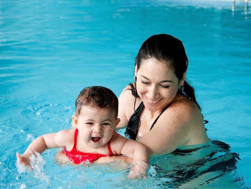 Parent holding a young smiling toddler in a pool